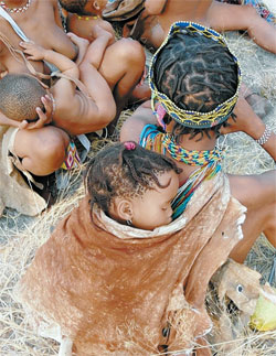 Familienrast: Ein Kind schläft auf dem Rücken der Mutter imTragetuch, ein anderes wird gefüttert.